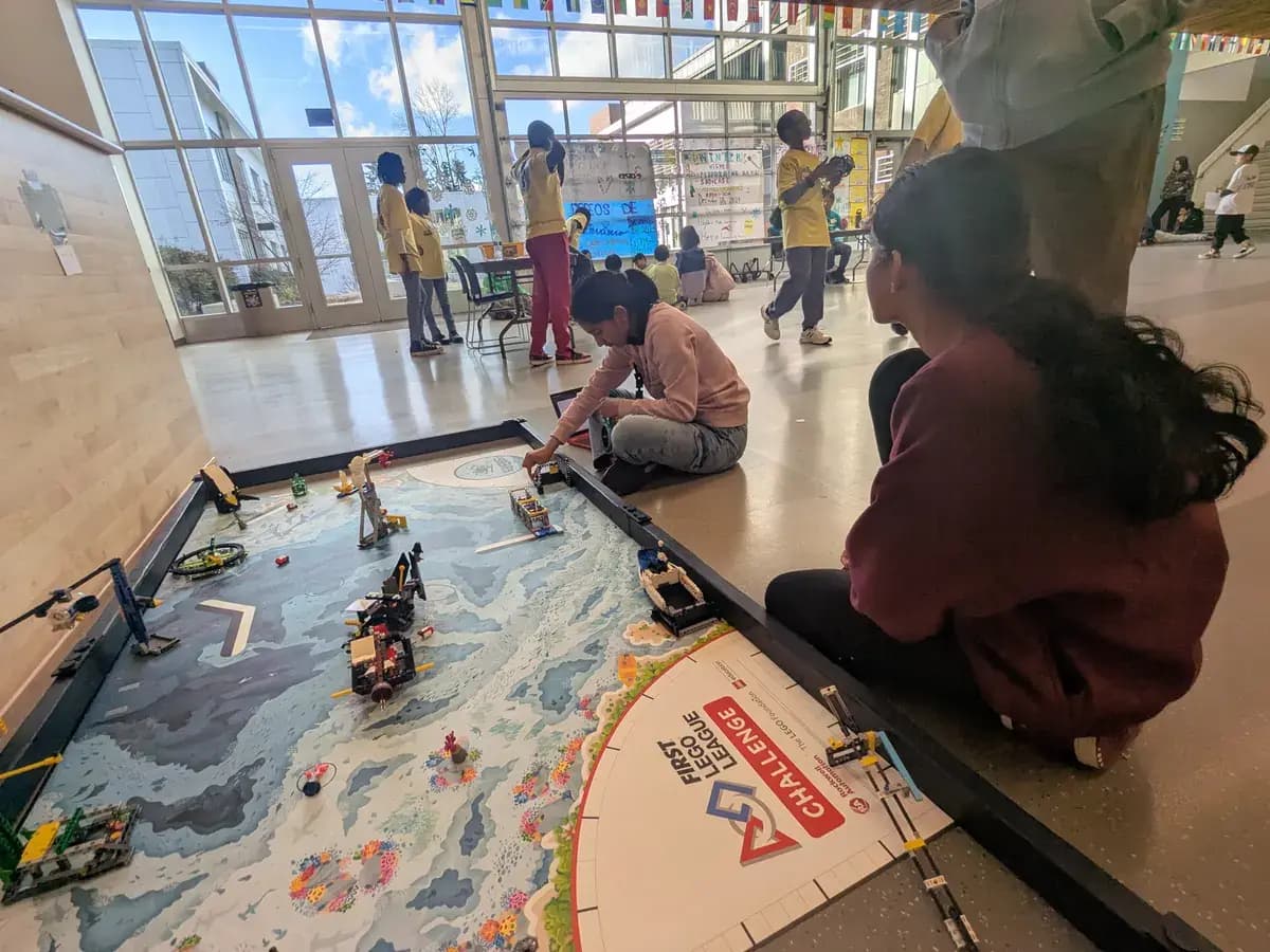 Students at a FIRST LEGO League competition, guiding their robots across the challenge mat