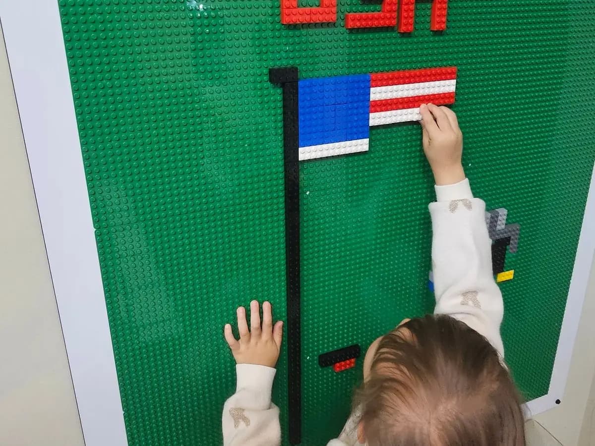 A preschooler's hands placing bricks on the classroom LEGO wall flag